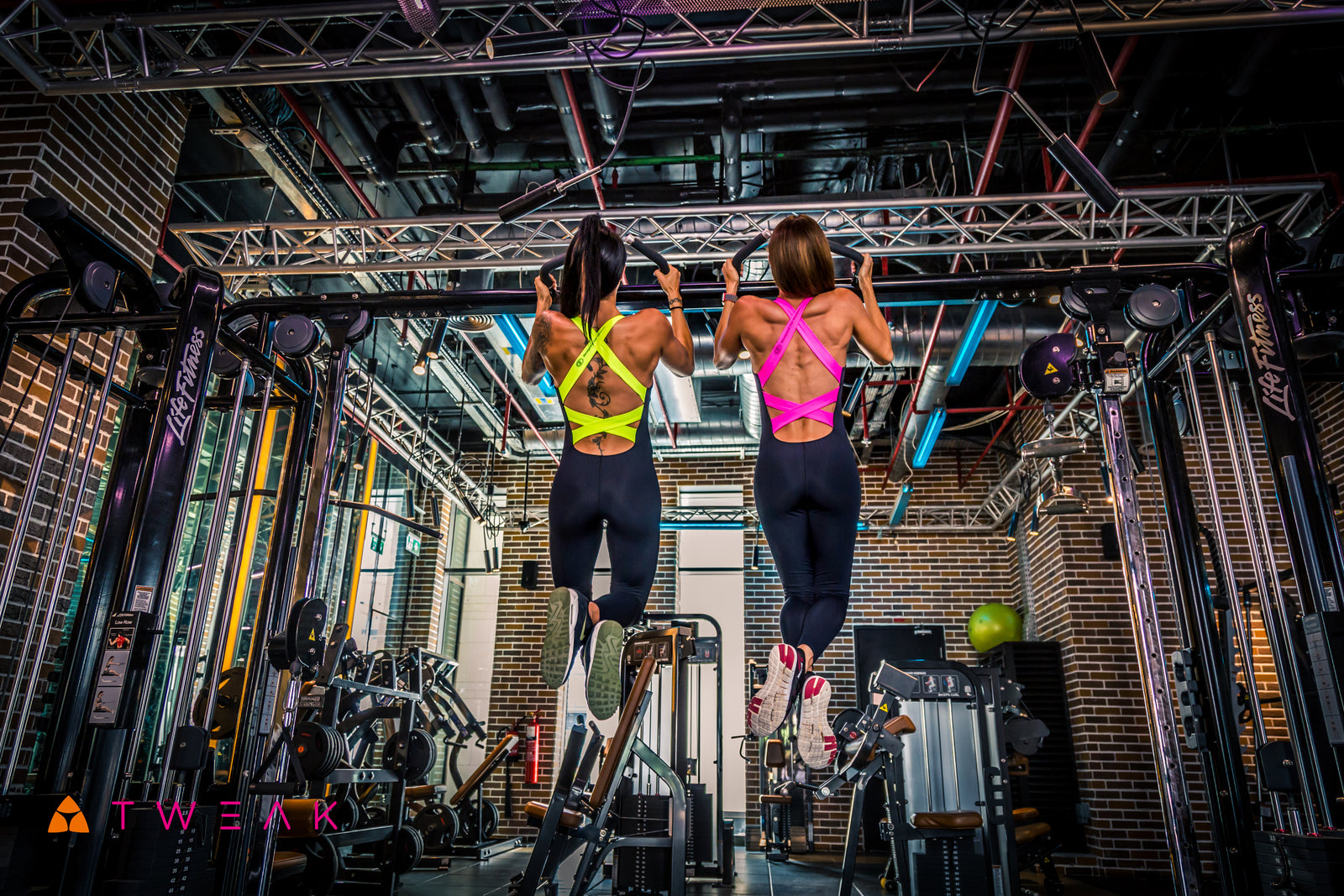 Two women exercising on a pull-up bar in a gym setting.